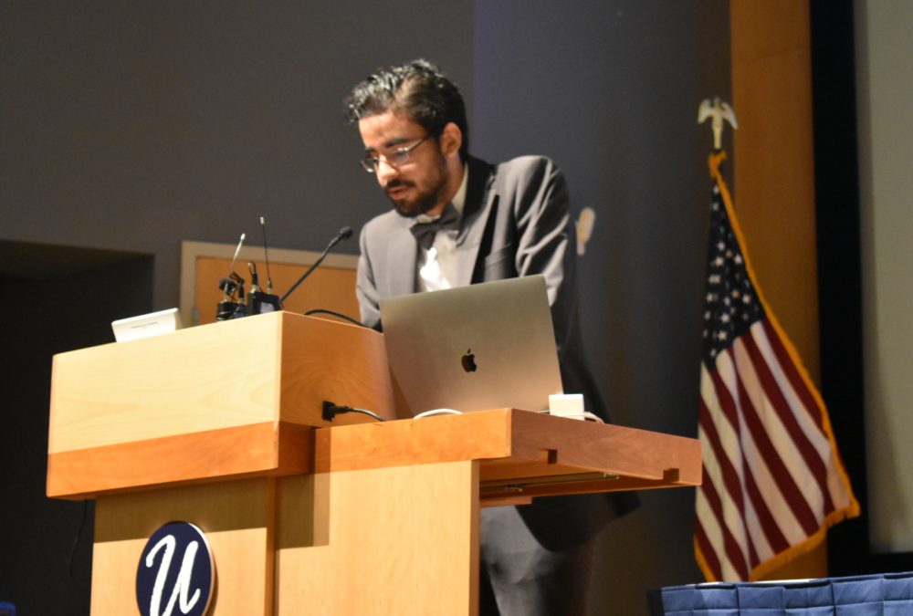 male with a beard at a podium speaking
