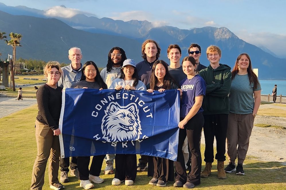 uconn students holding a uconn husky flag in taiwan (republic of china) with mountains in the background